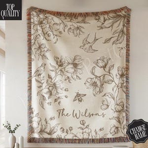 May include: Beige throw blanket with a floral and bird design. The throw features a fringe border and the text "The Wilsons". The blanket is hanging on a wall. The words "Top Quality" and "Change Name" are also visible.