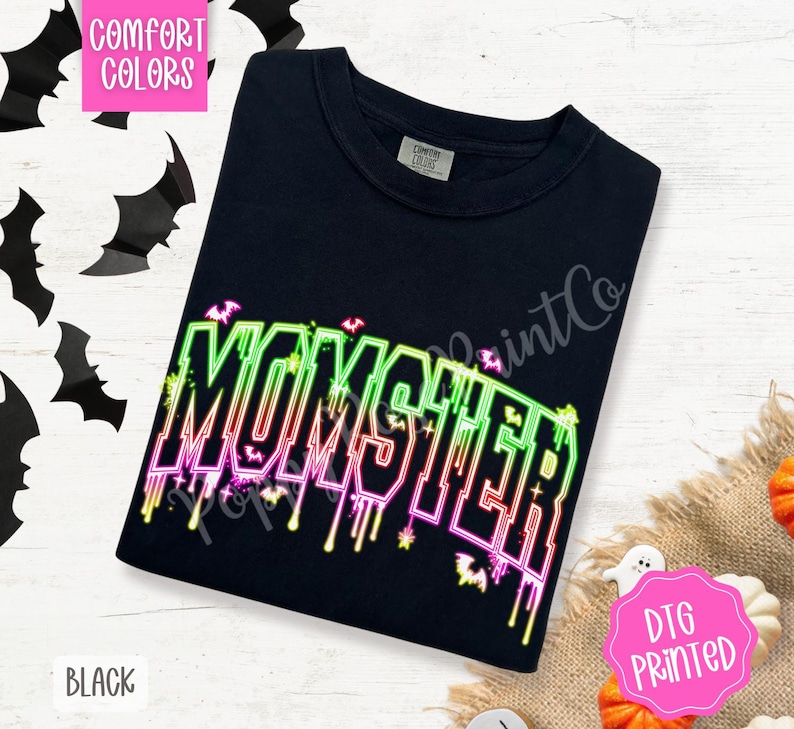 May include: Black t-shirt with the word "MONSTER" in neon green, pink, and yellow. The word has a dripping effect and is decorated with bats. The shirt is labeled "Comfort Colors" and "DTG Printed".