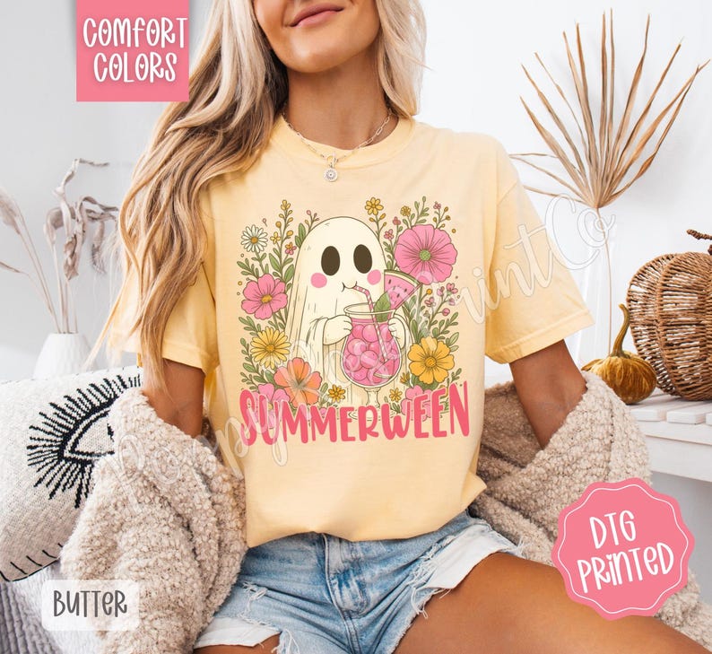 May include: Yellow t-shirt with a graphic of a ghost holding a pink drink, surrounded by flowers. The word "SUMMERWEEN" is printed in pink. The shirt has the words "COMFORT COLORS" and "BUTTER" printed on it.