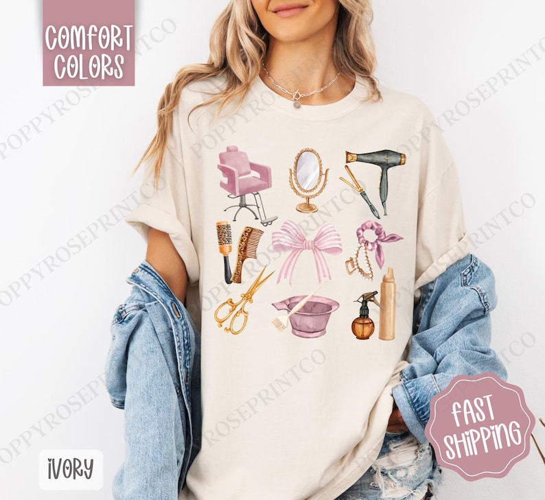 May include: A beige t-shirt with a design of various hair salon tools, including a pink salon chair, a hairdryer, scissors, combs, a hairspray bottle, and a pink hair dye bowl. The design is in a watercolor style with gold accents.