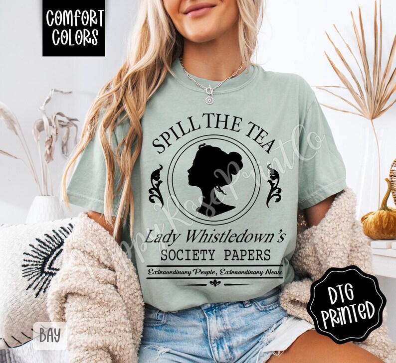 Pu&ograve; includere: T-shirt verde chiaro con la scritta "SPILL THE TEA" sopra una silhouette di profilo femminile. Sotto, si legge "Lady Whistledown's SOCIETY PAPERS". La maglietta ha anche le parole "COMFORT COLORS" e "DTG PRINTED".