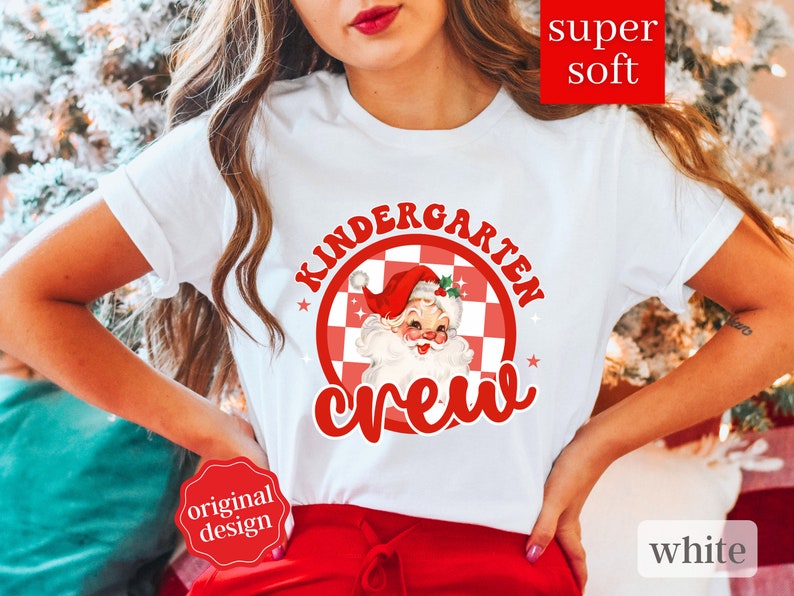May include: White t-shirt with a red and white checkered circle design featuring a cartoon Santa Claus with the text "Kindergarten Crew".
