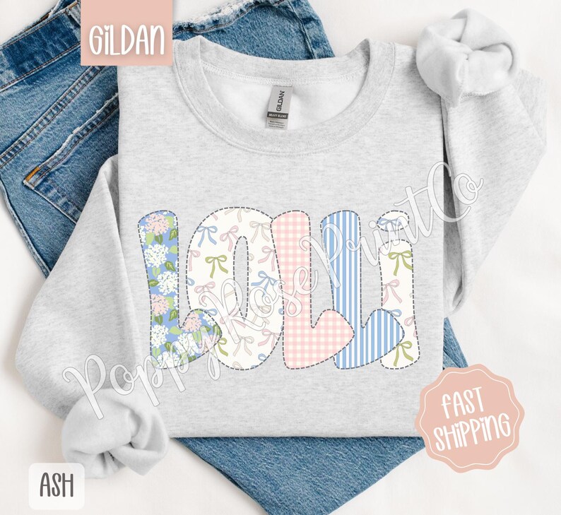 May include: A light gray sweatshirt with the word "LOLI" spelled out in colorful patchwork letters. The letters are made of different fabrics with floral, plaid, and striped patterns. The sweatshirt is a Gildan brand.