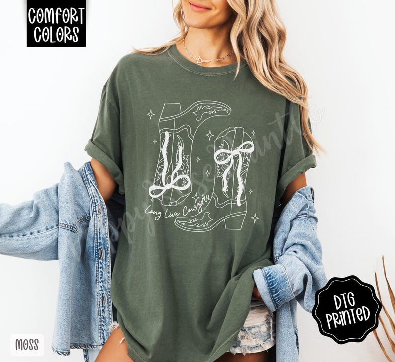 May include: Moss green t-shirt with a white graphic of two cowboy boots and the text "Long Live Cowgirls". The shirt is a Comfort Colors brand and has a relaxed fit. The design is DTG printed.