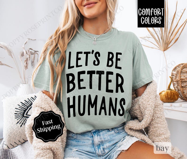 May include: A light green t-shirt with the text "Let's Be Better Humans" printed in black. The shirt is being worn by a person.