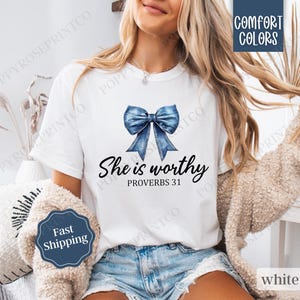 May include: White t-shirt with a blue denim bow and the text "She is worthy Proverbs 31" printed on the front.