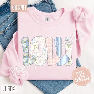 May include: A light pink Gildan sweatshirt with the word "LOLI" spelled out in colorful patchwork letters. The letters are made of different fabrics with floral, gingham, and striped patterns.