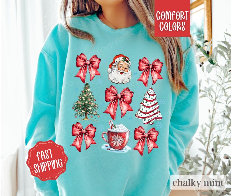 May include: A turquoise blue sweatshirt with a Christmas theme featuring Santa Claus, Christmas trees, bows, and a cup of hot chocolate. The text "COMFORT COLORS" is in the top right corner and "chalky mint" is in the bottom right corner.