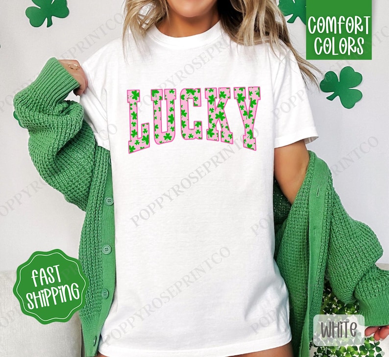 May include: White t-shirt with a pink "LUCKY" graphic. The letters are filled with a pattern of green shamrocks.