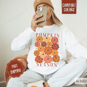 May include: White sweatshirt with a graphic print of orange, red, and brown pumpkins and the text "Pumpkin Season".