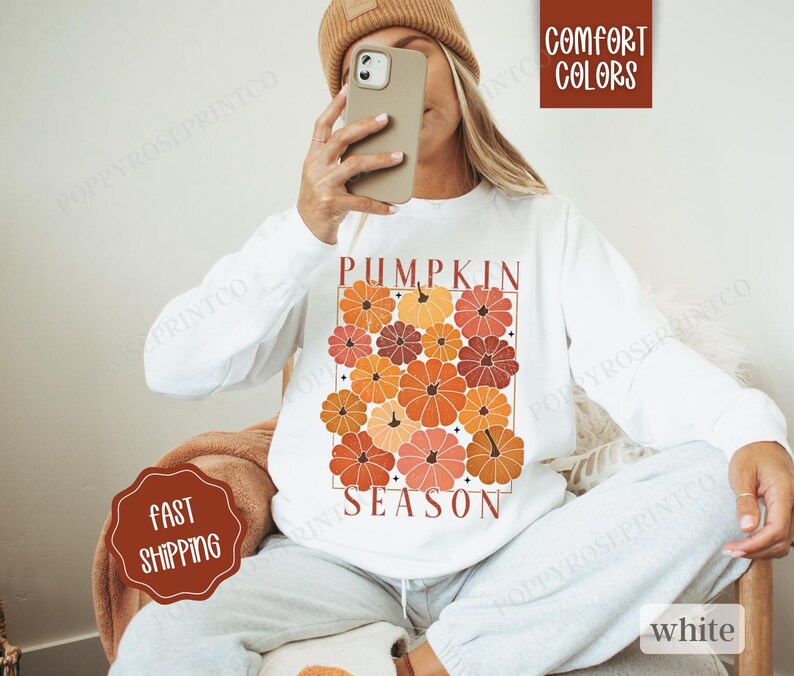 May include: White sweatshirt with a graphic print of orange, red, and brown pumpkins and the text "Pumpkin Season".