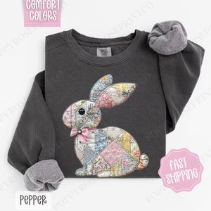 May include: A charcoal gray sweatshirt with a patchwork bunny design. The bunny is made of pink, blue, and green fabric with a pink bow. The sweatshirt has the word "Pepper" printed on the bottom.