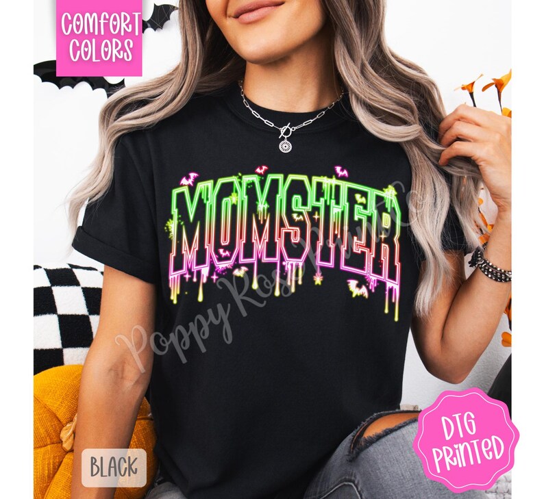 May include: Black t-shirt with the word "MOMSTER" in neon green and pink, with dripping accents and bat graphics. The shirt is labeled "Comfort Colors" and "DTG Printed".