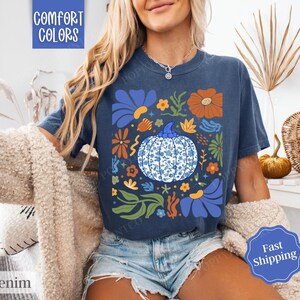 Op de afbeelding: Een marineblauw T-shirt met een bloemenpatroon met een blauwe en witte pompoen. De tekst "Comfort Colors" is zichtbaar in de linkerbovenhoek van de afbeelding.