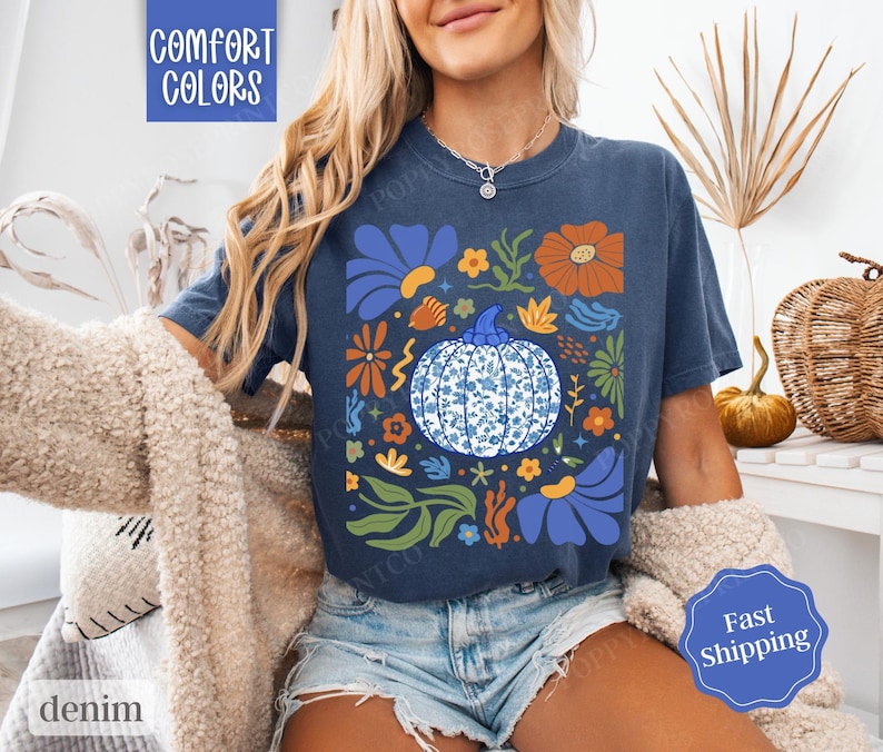 Op de afbeelding: Een marineblauw T-shirt met een bloemenpatroon met een blauwe en witte pompoen. De tekst "Comfort Colors" is zichtbaar in de linkerbovenhoek van de afbeelding.