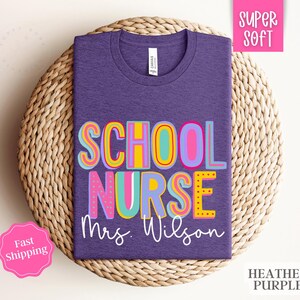 Puede incluir: Camiseta morada con el texto "School Nurse Mrs. Wilson" en letras coloridas y divertidas. La camiseta est&aacute; hecha de una tela suave y c&oacute;moda.