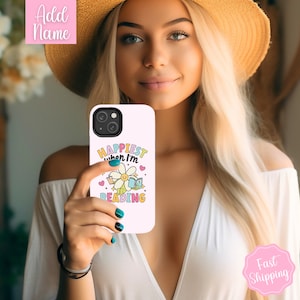 May include: White phone case with a colorful graphic that says "Happiest when I'm reading" with a daisy and books.