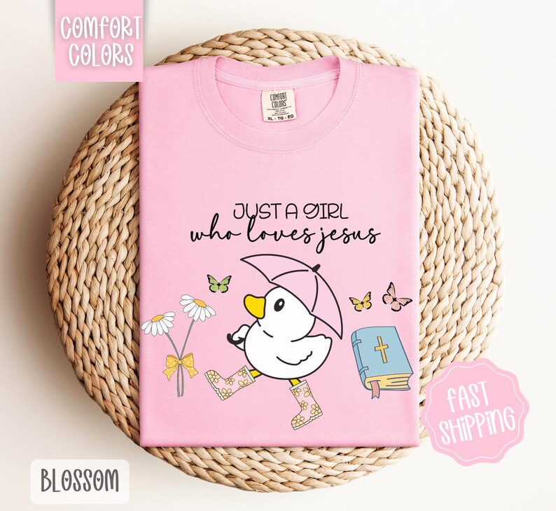 Puede incluir: Camiseta rosa con un pato de dibujos animados que lleva botas de lluvia y sostiene un paraguas. La camiseta tiene el texto "Just a girl who loves Jesus" y una imagen de una biblia.