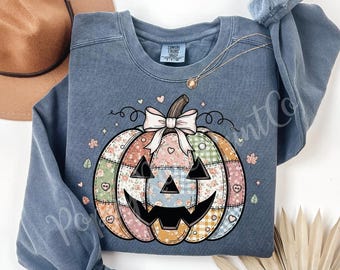 May include: Blue jean-coloured sweatshirt with a patchwork pumpkin design. The pumpkin has a smiling jack-o'-lantern face, a white bow, and floral and heart accents. The text "BLUE JEAN" is visible.