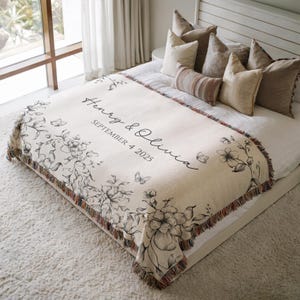 May include: Cream-coloured throw blanket with a floral and butterfly design. The blanket has a fringed edge and features the names "Henry & Olivia" and the date "SEPTEMBER 4 2025" in black script.