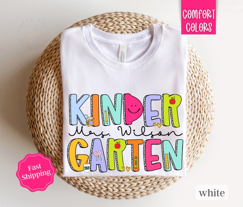 May include: White t-shirt with a colorful graphic that says "Kinder Mrs. Wilson Garten".