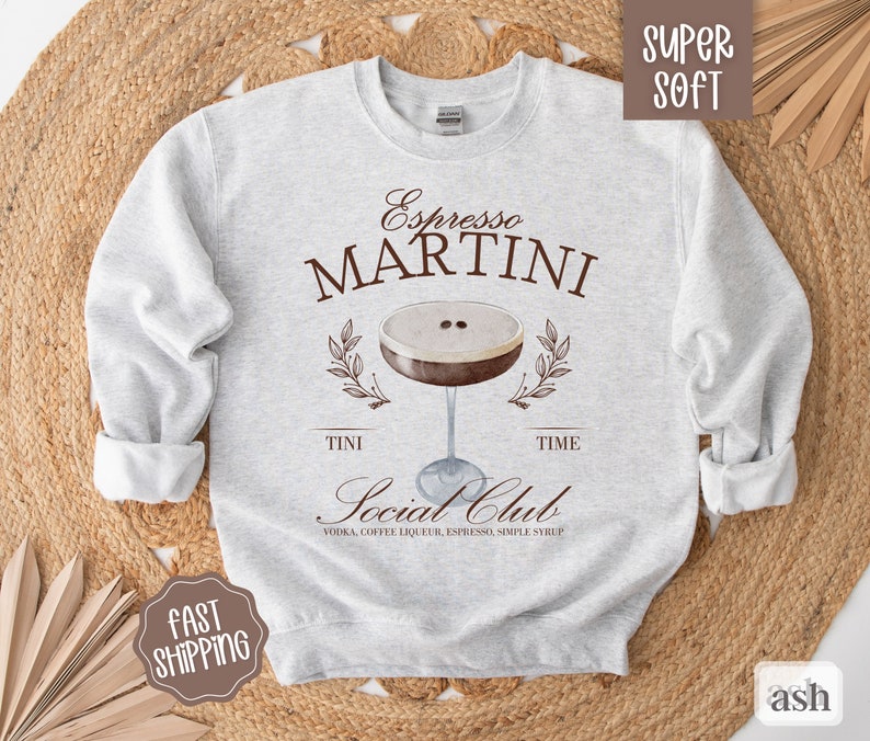 May include: Gray sweatshirt with the text "Espresso MARTINI" and a graphic of a martini glass with coffee beans. The text "TINI TIME Social Club VODKA, COFFEE LIQUEUR, ESPRESSO, SIMPLE SYRUP" is below the graphic.