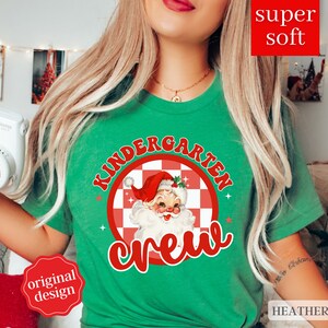 May include: Green t-shirt with a red and white checkered circle featuring a cartoon Santa Claus and the text "Kindergarten Crew".