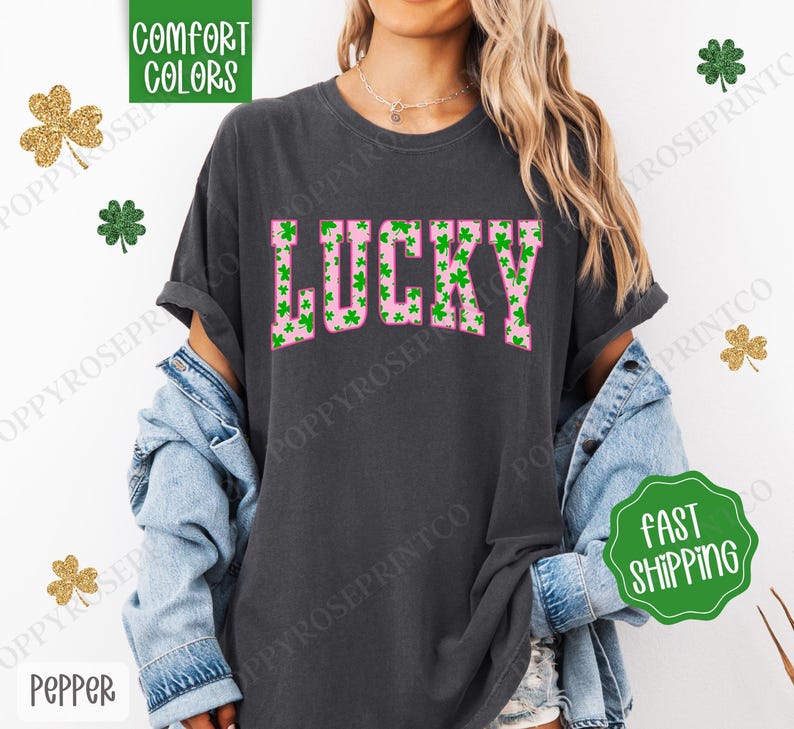 May include: A dark gray t-shirt with a pink "LUCKY" graphic. The letters are filled with green shamrock patterns.