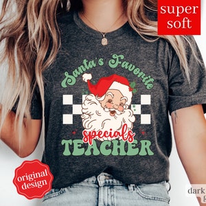 Pode incluir: Uma camiseta cinza escuro com um design retrô que apresenta o Papai Noel e o texto "Santa's Favorite Specials Teacher".