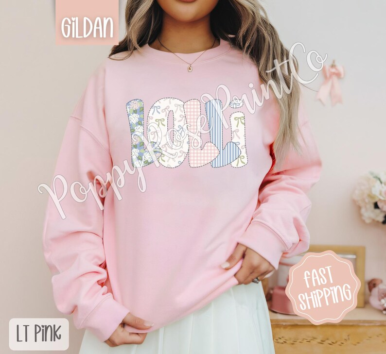 May include: A light pink sweatshirt with the word "LOLI" spelled out in colorful patchwork letters. The letters are decorated with floral and heart patterns.