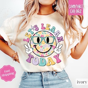 May include: A white t-shirt with a colorful graphic of a smiling face wearing sunglasses and the text "Let's Learn Today".