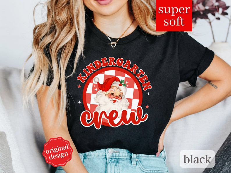 May include: Black t-shirt with a red and white checkered circle design featuring a cartoon Santa Claus and the text "Kindergarten Crew".