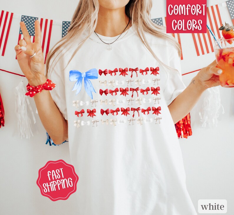 May include: White t-shirt featuring a design of the American flag made of bows. The flag design includes a large blue bow in the upper left corner, with red and white bows arranged in rows. The words "Comfort Colors" are in a red box in the upper right corner.