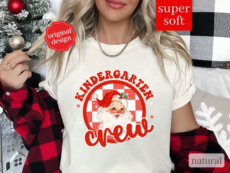 May include: White t-shirt with red text that says "Kindergarten Crew" and a red and white checkered circle with a cartoon Santa Claus inside.