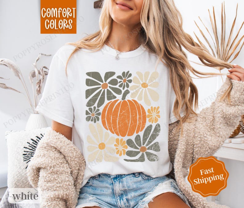 Puede incluir: Camiseta blanca con un dise&ntilde;o gr&aacute;fico de una calabaza y flores en tonos verdes, amarillos y naranjas. El texto "Comfort Colors" es visible en la esquina superior izquierda de la imagen.
