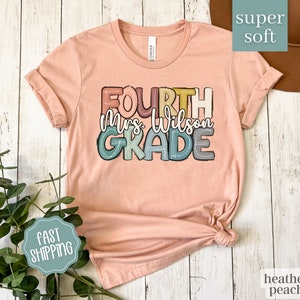 May include: A peach colored t-shirt with the text "FOURTH Mrs. Wilson GRADE" in colorful, outlined letters. The shirt is made of a soft, comfortable fabric.