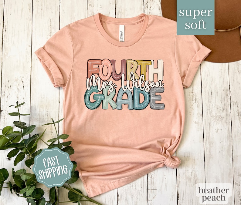 May include: A peach colored t-shirt with the text "FOURTH Mrs. Wilson GRADE" in colorful, outlined letters. The shirt is made of a soft, comfortable fabric.
