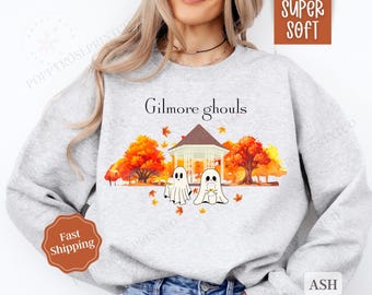 May include: A gray sweatshirt with the text "Gilmore ghouls" printed on the front. The design features two ghosts holding pumpkins in front of a gazebo with fall foliage.