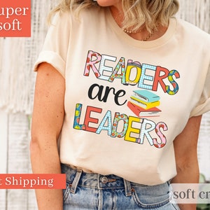 May include: A cream colored t-shirt with the text "Readers are Leaders" in colorful letters with a stack of books in the middle. The letters are decorated with different patterns.