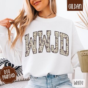 May include: White sweatshirt with the letters WWJD in a camouflage pattern across the chest. The sweatshirt is a Gildan brand and has a crew neck. The words "DTG Printed" are on a brown sticker.