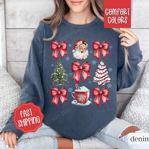 May include: A navy blue sweatshirt with a Christmas theme featuring Santa Claus, Christmas trees, and red bows. The text "Comfort Colors" is printed on the top right corner of the sweatshirt.