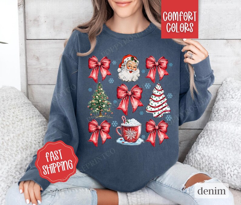 May include: A navy blue sweatshirt with a Christmas theme featuring Santa Claus, Christmas trees, and red bows. The text "Comfort Colors" is printed on the top right corner of the sweatshirt.