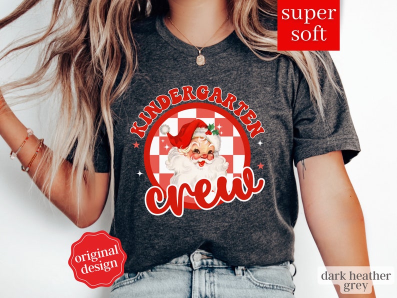 May include: Dark heather grey t-shirt with a red and white checkered circle design featuring a vintage Santa Claus illustration and the text "Kindergarten Crew".