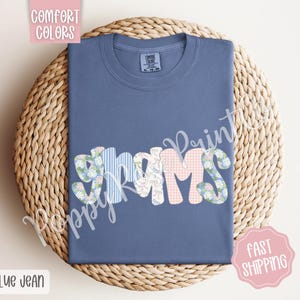May include: A blue jean t-shirt with the word "GRAMS" spelled out in colorful patchwork fabric letters.