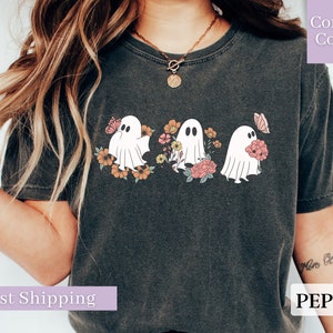 Peut inclure: Un t-shirt gris fonc&eacute; avec un motif de trois fant&ocirc;mes blancs tenant des fleurs. Les fant&ocirc;mes sont entour&eacute;s de fleurs roses, orange et jaunes. Le t-shirt a un col rond et des manches courtes.