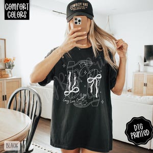 May include: Black t-shirt with a white graphic of two cowboy boots and the text "Long Live Cowboys". The shirt also has the text "Comfort Colors" and "DTG Printed".