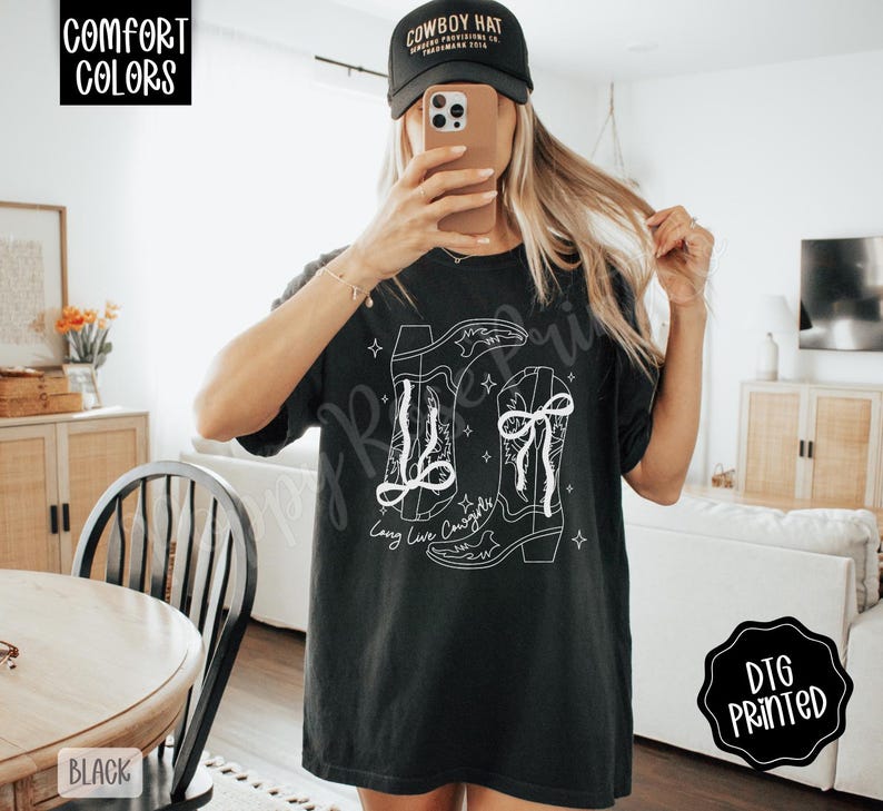 May include: Black t-shirt with a white graphic of two cowboy boots and the text "Long Live Cowboys". The shirt also has the text "Comfort Colors" and "DTG Printed".
