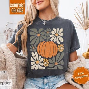 Puede incluir: Una camiseta gris oscuro con un gr&aacute;fico de estilo vintage de una calabaza rodeada de flores. El texto "Comfort Colors" es visible en la esquina superior izquierda de la imagen.