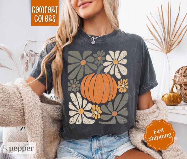 Puede incluir: Una camiseta gris oscuro con un gr&aacute;fico de estilo vintage de una calabaza rodeada de flores. El texto "Comfort Colors" es visible en la esquina superior izquierda de la imagen.
