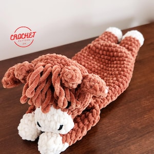 May include: A brown and white crocheted stuffed animal resembling a horse lying on its side. The animal has a fluffy mane and tail.